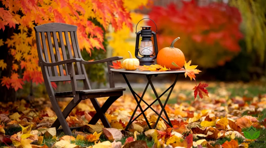 A photo of a cozy outdoor setting with a wooden chair and a small table. On the table, there is a lantern, a pumpkin, and a few autumn leaves. The background is a garden with vibrant autumn leaves in shades of orange, yellow, and red. The ground is covered with fallen leaves. The overall image has a warm color scheme palette.